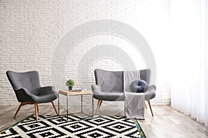 Stylish sofa and armchair near brick wall in modern living room interior