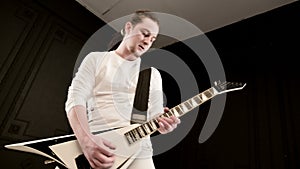 Stylish solo guitarist with dreadlocks on his head and in white clothes on a black background expressively playing the