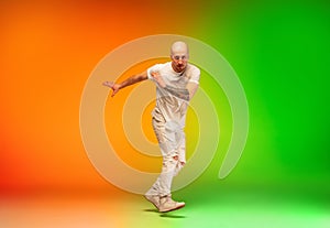 Stylish sportive caucasian man dancing hip-hop on colorful gradient background at dance hall in neon light.