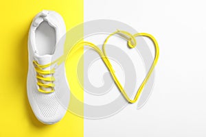 Stylish sportive shoe and yellow laces in shape of heart on color background, flat lay