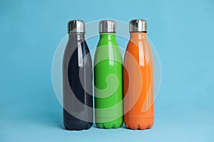 Stylish stainless thermo bottles on light blue background