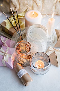 Stylish still life with gift boxes, candle sticks, burning candles, garland on light windowsill background, boho romance concept