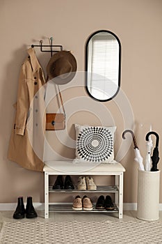 Stylish storage bench with different pairs of shoes near beige wall in hall