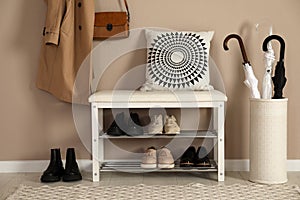 Stylish storage bench with different pairs of shoes near beige wall in hall