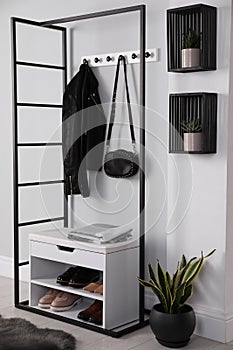 Stylish storage cabinet with different pairs of shoes near white wall in hall