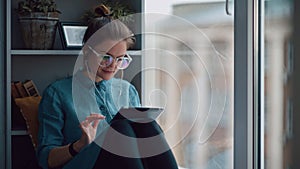 Stylish student girl sits by the window on windowsill with a gadget