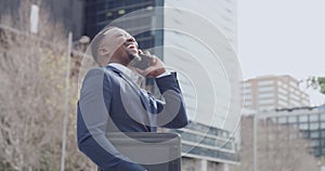 Stylish and successful businessman talking on a phone call, laughing while networking on a cellphone alone in the city
