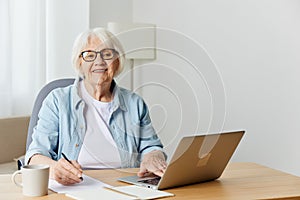 a stylish, successful elderly woman with gray hair works from home on a laptop and looks at the camera with a pleasant