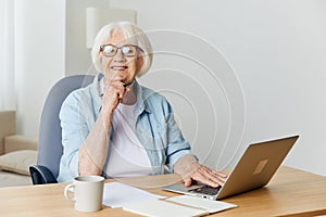 a stylish, successful elderly woman with gray hair works from home on a laptop and looks at the camera with a pleasant