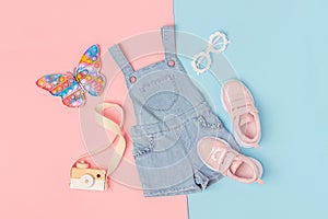 Stylish summer set of child clothes. Denim jumpsuit, pink sneakers and accessories on a pink blue background. Fashion