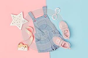 Stylish summer set of child clothes. Denim jumpsuit, pink sneakers and accessories on a pink blue background. Fashion