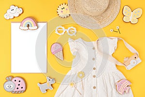 Stylish summer set of child clothes. White blank card, cotton dress, straw hat, sunglasses and funny cookies gingerbread on yellow