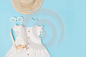 Stylish summer set of child clothes. White dress, the straw hat, sunglasses and accessories on blue background. Fashion girl