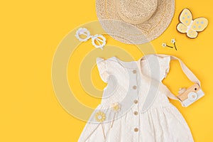 Stylish summer set of child clothes. White dress, the straw hat, sunglasses and accessories on yellow background. Fashion girl