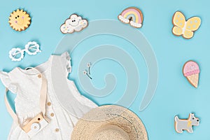 Stylish summer set of child clothes. White dress, the straw hat, sunglasses and funny gingerbread on blue background. Fashion girl