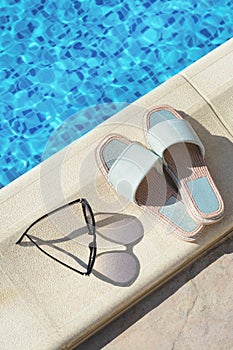 Stylish sunglasses and slippers at poolside on sunny day. Beach accessories