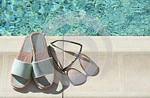 Stylish sunglasses and slippers at poolside on sunny day, space for text. Beach accessories