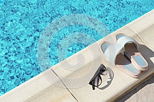 Stylish sunglasses and slippers at poolside on sunny day, space for text. Beach accessories