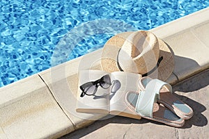 Stylish sunglasses, slippers, straw hat and book at poolside on sunny day. Beach accessories