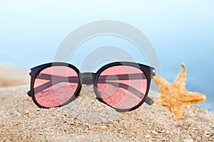 Stylish sunglasses and starfish on sandy beach