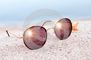Stylish sunglasses and starfish on sandy beach near sea, closeup