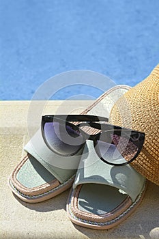 Stylish sunglasses, visor cap and slippers at poolside on sunny day. Beach accessories