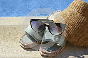 Stylish sunglasses, visor cap and slippers at poolside on sunny day. Beach accessories