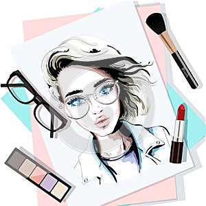 Stylish table set with hand drawn woman portrait, papers, lipstick, eyeglasses, brush and eyeshadows. Sketch.