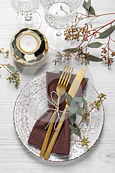 Stylish table setting with cutlery, burning candle and eucalyptus leaves, flat lay