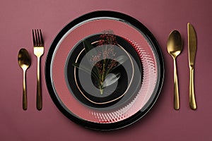 Stylish table setting with cutlery and floral decor on pink background, flat lay