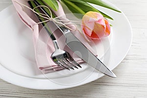 Stylish table setting with cutlery and tulip on white wooden background, closeup