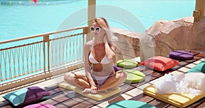 Stylish tanned woman sitting with crossed legs on colorful pillows at open terrace