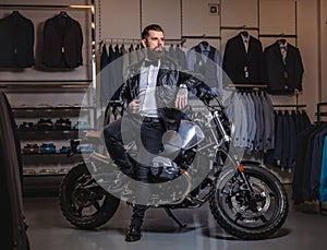 Stylish tattooed bearded man with dressed in black leather jacket and bow tie posing near retro sports motorbike at men