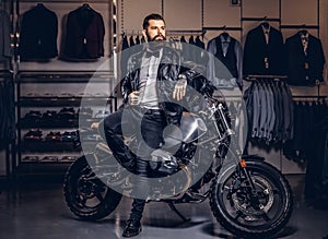 Stylish tattooed bearded man with dressed in black leather jacket and bow tie posing near retro sports motorbike at men