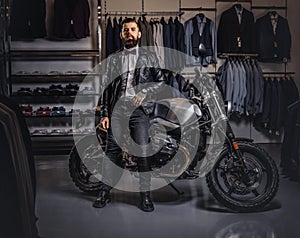 Stylish tattooed bearded man with dressed in black leather jacket and bow tie posing near retro sports motorbike at men