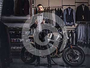 Stylish tattooed bearded man with dressed in black leather jacket and bow tie posing near retro sports motorbike at men