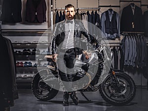 Stylish tattooed bearded man with dressed in black leather jacket and bow tie posing near retro sports motorbike at men