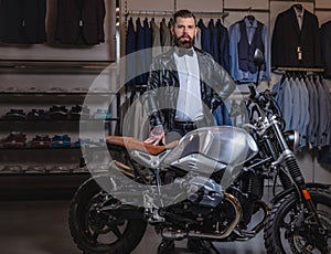 Stylish tattooed bearded man with dressed in black leather jacket and bow tie posing near retro sports motorbike at men