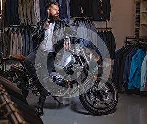 Stylish tattooed bearded man with dressed in black leather jacket and bow tie posing near retro sports motorbike at men