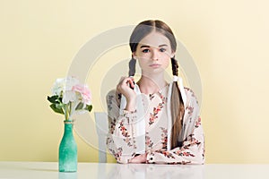 stylish teen girl with braids sitting at table with vase and flowers
