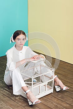 stylish teen girl with parrot in cage sitting
