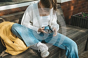 A stylish teenage girl engrossed in her smartphone, sitting casually on a modern bench