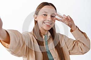 Stylish teenage girl, female student posing with v-sign for selfie, holding smartphone, taking picture on mobile phone