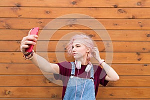 Stylish teenage girl with pink hair and headphones stylish clothes to make selfie smartphone