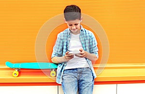 Stylish teenager boy with skateboard using smartphone in city