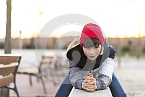 Stylish teenager with knit hat sitting on a fence in a city park