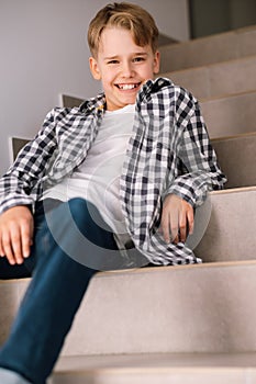 Stylish teenager laughs while looking at the camera. The guy is sitting on the steps indoors