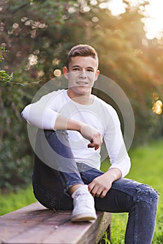 Stylish teenager sitting on a wooden bench on a city park