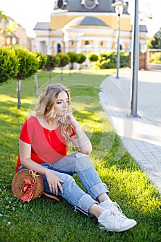 Stylish teenager weared in jeans and red T-shirt sitting on grass.