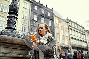 Stylish tourist in the city in the cold season is looking for directions on a mobile phone.